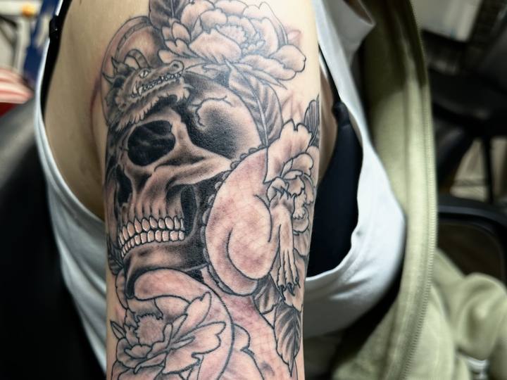 Black and grey skull with peonies on an upper arm